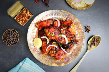 Tandoori chicken is a popular roast chicken recipe from India.   Tandoor is a traditional wood oven. Chicken Tandoori Platter is served in a brass plate with salad and spices. Copy Space.  - obrazy, fototapety, plakaty