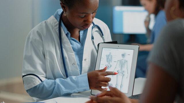Woman working as doctor holding tablet with skeleton image for osteopathy diagnosis. Medic explaining human bones structure and anatomy for orthopedic examination on modern gadget.