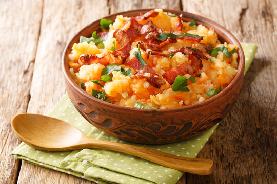 Hutspot is a traditional Dutch one pot meal of mashed potatoes, carrots and onions with fried bacon close up in the pan on the table. Horizontal