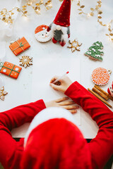 cute little boy in red sweater and Santa hat writes letter to Santa Claus asking to bring presents, top view, New Year and Christmas concept, DIY child, kid believes in miracles