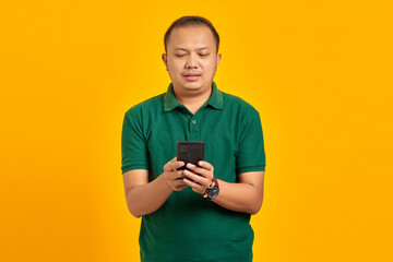 Portrait of smiling young Asian man using a mobile phone on yellow background