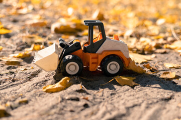 Orange toy bulldozer on the sand with yellow leaves