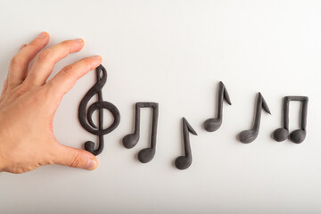 Mans hand holds violin key and notes on white background. Treble clef. Key of G.