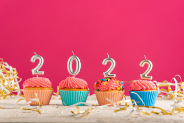 Festive cupcakes and candles in form of numbers 2022 on pink background. Concept of New year.