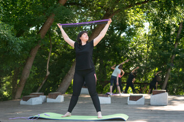 Young woman coach shows how to do with the help of an expander and pump up arms. Purple expander....