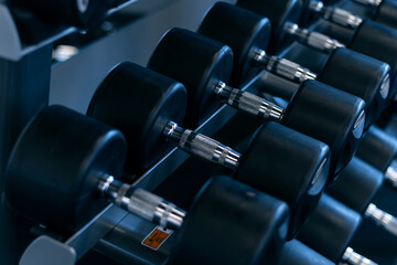 Black dumbbells in the gym. Sports equipment. Lots of metal dumbbells on the counter in the sports...