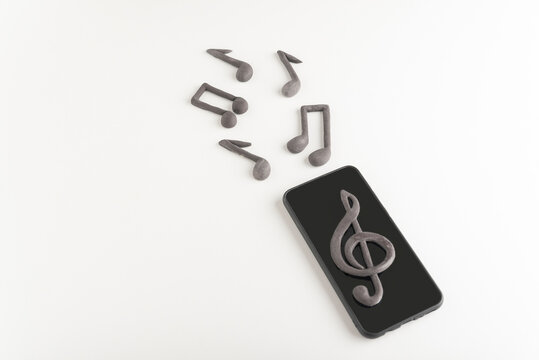 Mobile phone with treble clef on display and musical notes on white background. Application to listen music on your phone.