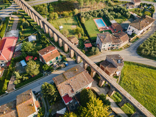Aerial view of an old aqueduct and rooftops in Italian village. Roman arches irrigation historical landmark. Acquedotto del Nottolini Lucca Toscana