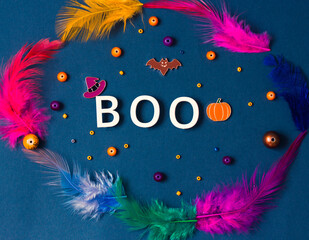 Boo word, colorful feathers on dark grey background. Halloween holiday concept. Bat, orange jack o lantern pumpkin, witch hat symbols. Party greeting card. Copy space, place for text. Flatly top view.