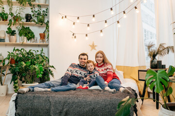 Happy family in Christmas sweaters on bed.