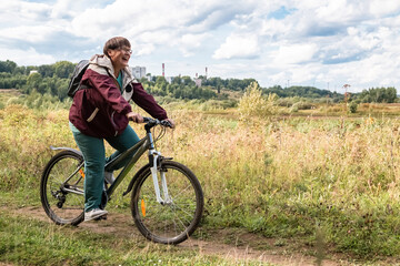 Fototapeta premium Cheerful grandmother rides a bicycle in nature.