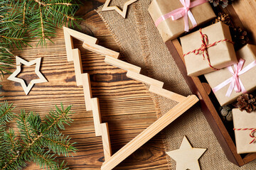 Wooden christmas tree with gift boxes, fir branches, pine cones and wooden stars on wooden background