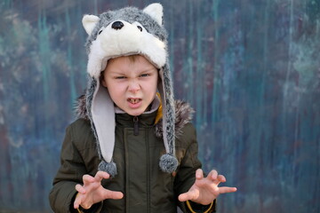 The roar of a wolf. Child in a wolf hat on gray background, outdoor.