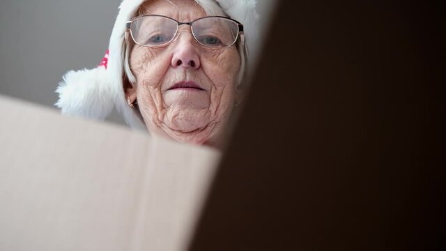 Happy surprised senior woman wearing santa hat hold open gift box. smiling elderly grandma customer receive post shipment online shop. woman opening gift from the box view. fast delivery christmas