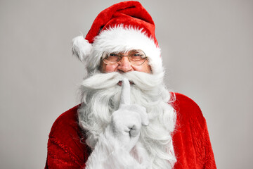 Santa Claus standing on the grey background and showing quiet sign