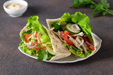 Pita stuffed with chicken, pepper, cucumber and lettuce on white plate. Eastern cuisine