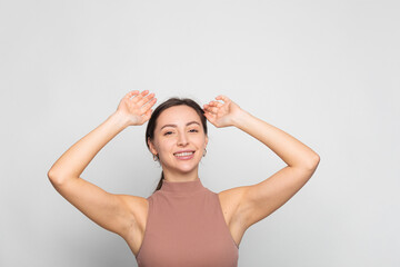 Fototapeta na wymiar Young woman overjoyed with two hands raised and celebrating victory while standing on grey background copy space
