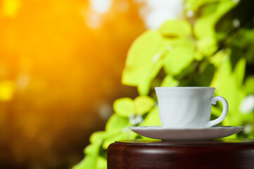 White cup of coffee or tea on a wooden table over blurred tree with sun lighting