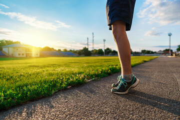 teen boy boy does physical exercises at the stadium track, close view of the legs, a soccer field with green grass - concept of sports and health