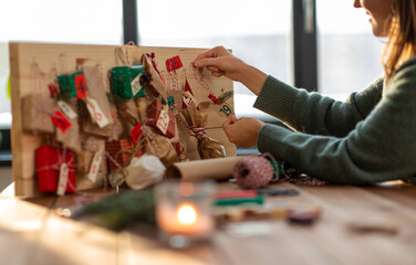 winter holidays, christmas and hobby concept - hands hanging gift with tag to handmade advent...