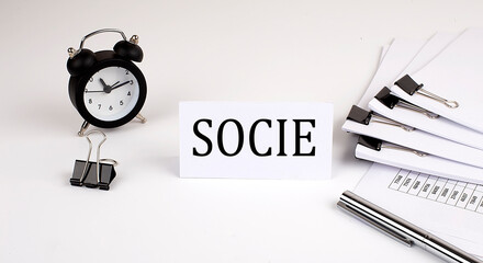 Card with text SOCIE on a white background, near office supplies and alarm clock. Business concept.