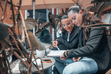 Secretarias jóvenes de pelo castaño revisando unas hojas de papel con informes y ideas de negocio para sus clientes en una cafetería de la ciudad	