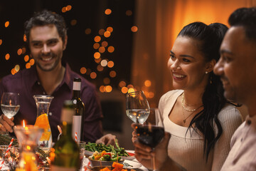 holidays and celebration concept - happy woman having christmas dinner with friends and drinking wine at home