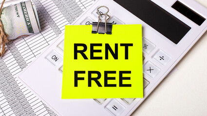 On a light background - cash, a white calculator and a yellow sticker under a black paper clip with the text RENT FREE. Business concept