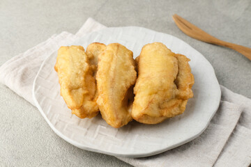 Pisang goreng or banana fritters (deep fried banana fritter with flour batter), served in white plate on grey background. Selective focus image. Close up.
