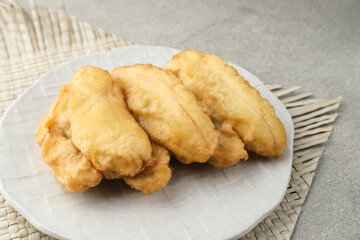 Pisang goreng or banana fritters (deep fried banana fritter with flour batter), served in white plate on grey background. Selective focus image. Close up.
