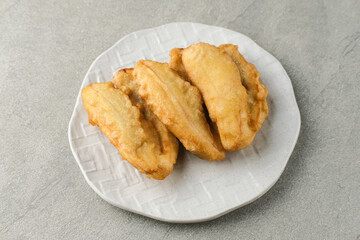 Pisang goreng or banana fritters (deep fried banana fritter with flour batter), served in white plate on grey background. Selective focus image. Close up.
