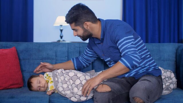 A loving father covering his little daughter sleeping on the sofa with a blanket. An attractive male with a beard gently patting a baby girl while sleeping - sound sleep  rhythmical movement  paren...