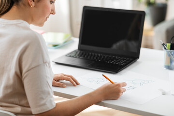 education, online school and distant learning concept - student woman with laptop computer drawing picture of cat on paper at home