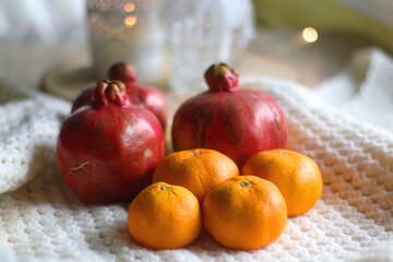 Fresh tangerines and pomegranates, soft blanket and lit candles. Selective focus.