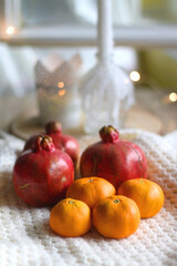 Fresh tangerines and pomegranates, soft blanket and lit candles. Selective focus.