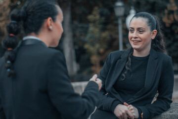 Secretarias de negocios de cabello oscuro y caucásicas charlando de relaciones laborables con una sonrisa de felicidad mientras gesticulan en una plaza de la ciudad fuera del trabajo