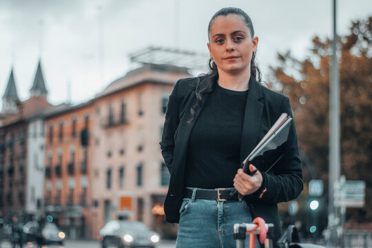 Gestora joven de cabello moreno formal con seriedad y de pie sujetando su tablet digital en el centro de la ciudad caminando por la calle para llegar a su trabajo