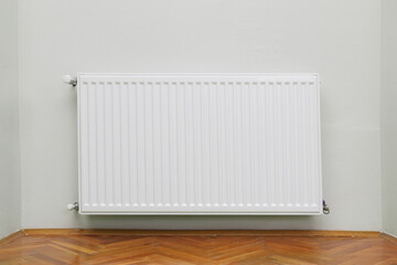 Home radiator heater on the white wall on wooden hardwood floor. Adjustable warming equipment for apartment and home 