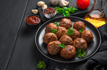Basil meatballs in a black plate on a dark background with sauce and spices.