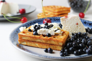 delicious healthy breakfast. Belgian soft waffles with curd cheese cream and blueberry cherries lie white blue plate view from the top. Delicious still life