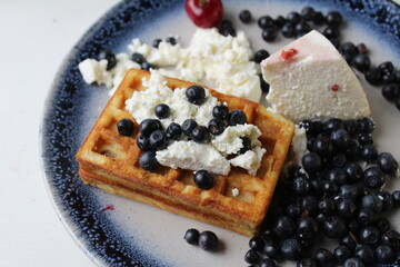 delicious healthy breakfast. Belgian soft waffles with curd cheese cream and blueberry cherries lie white blue plate view from the top. Delicious still life