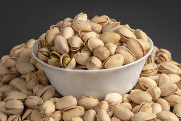 White bowl of pistachios on dark background