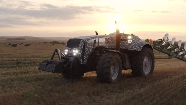 An Unmanned Tractor Drives Through A Field And Plows The Land With A Plow At Sunset