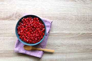 Bowl of fresh pomegranate seeds on wooden table. Top view.