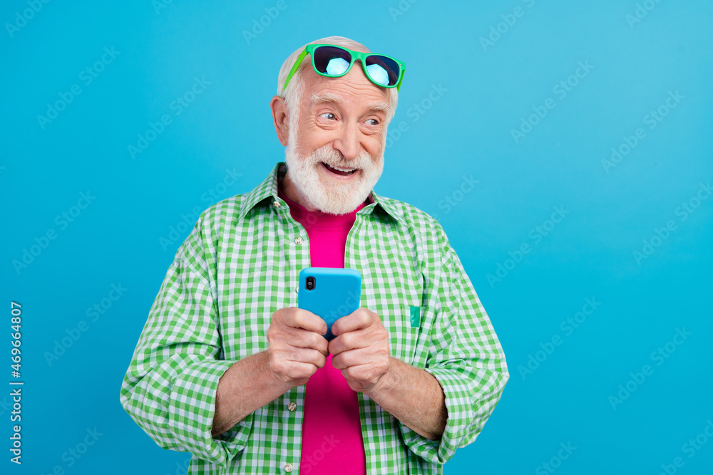 Sticker Photo of dreamy happy positive old granddad hold phone imagine comment media isolated on blue color background