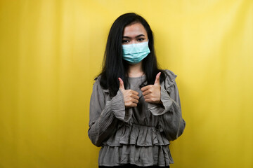 Beautiful young woman wearing a mask with thumbs up hands, okay hands, agreement, good work isolated