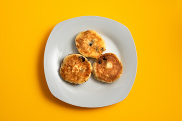 Three cottage cheese pancakes (syrniki) on white plate on yellow background
