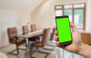 Man holding smartphone with blank chromakey screen to control electrical equipment in modern office