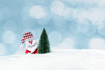 Santa Claus or Saint Nicholas near Christmas tree on natural snow on gentle blue background with bokeh and copy space. Merry Christmas, Happy New Year greeting card, banner, winter holidays concept