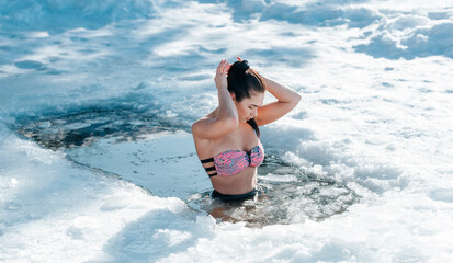 Girl with bikini and a watch in frozen lake ice hole. Woman hardening the body in cold water. Good...